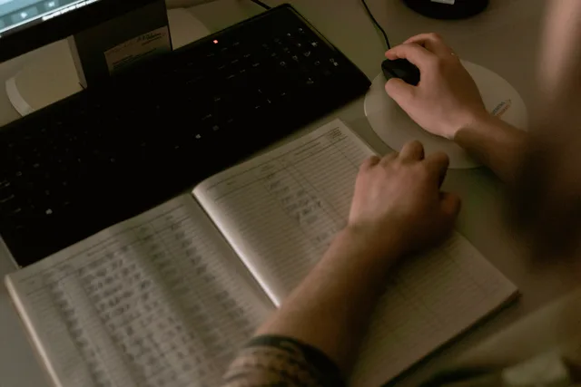 Healthcare worker reviewing medical data on a computer with a notebook open with written details, in a clinic setting. Så fungerar svenska adressregister för företag och fastigheter